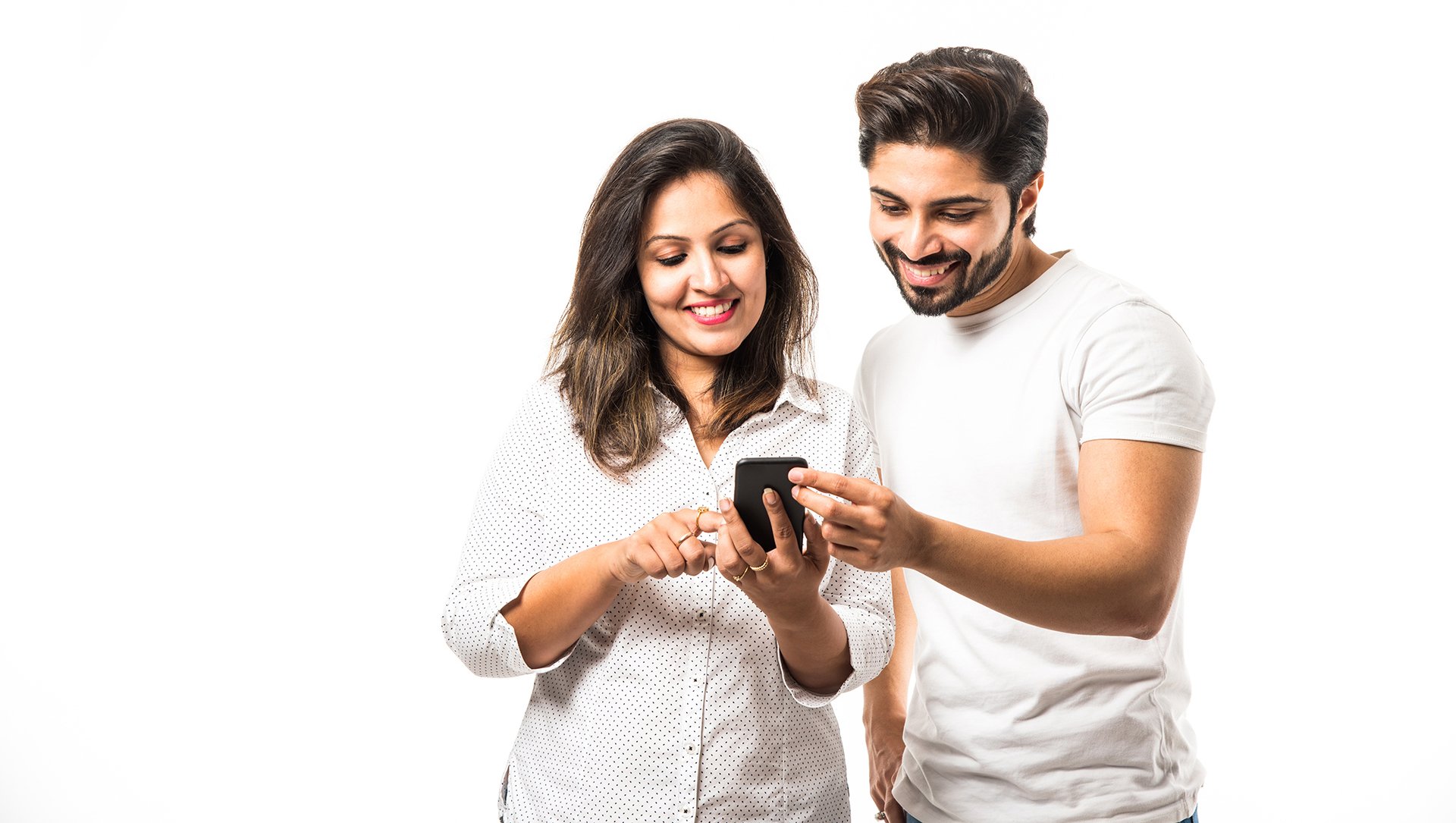 Indian young couple using smartphone or mobile handset, standing isolated over white background or against red brick background